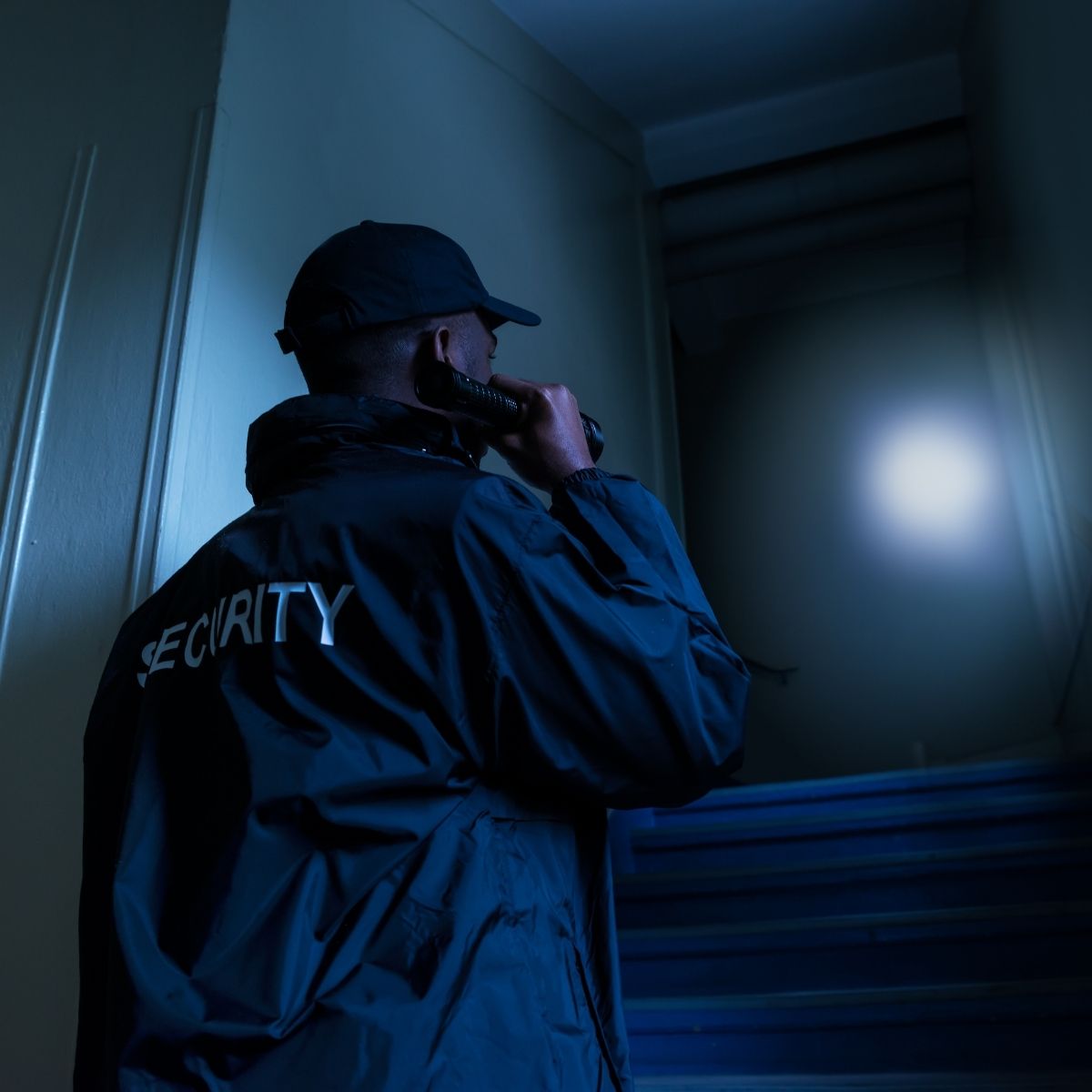 Un agent de sécurité privée en service lors d'une patrouille de nuit avec une lampe torche à la main. Un agent de sécurité en tenue lors d’une patrouille de nuit.